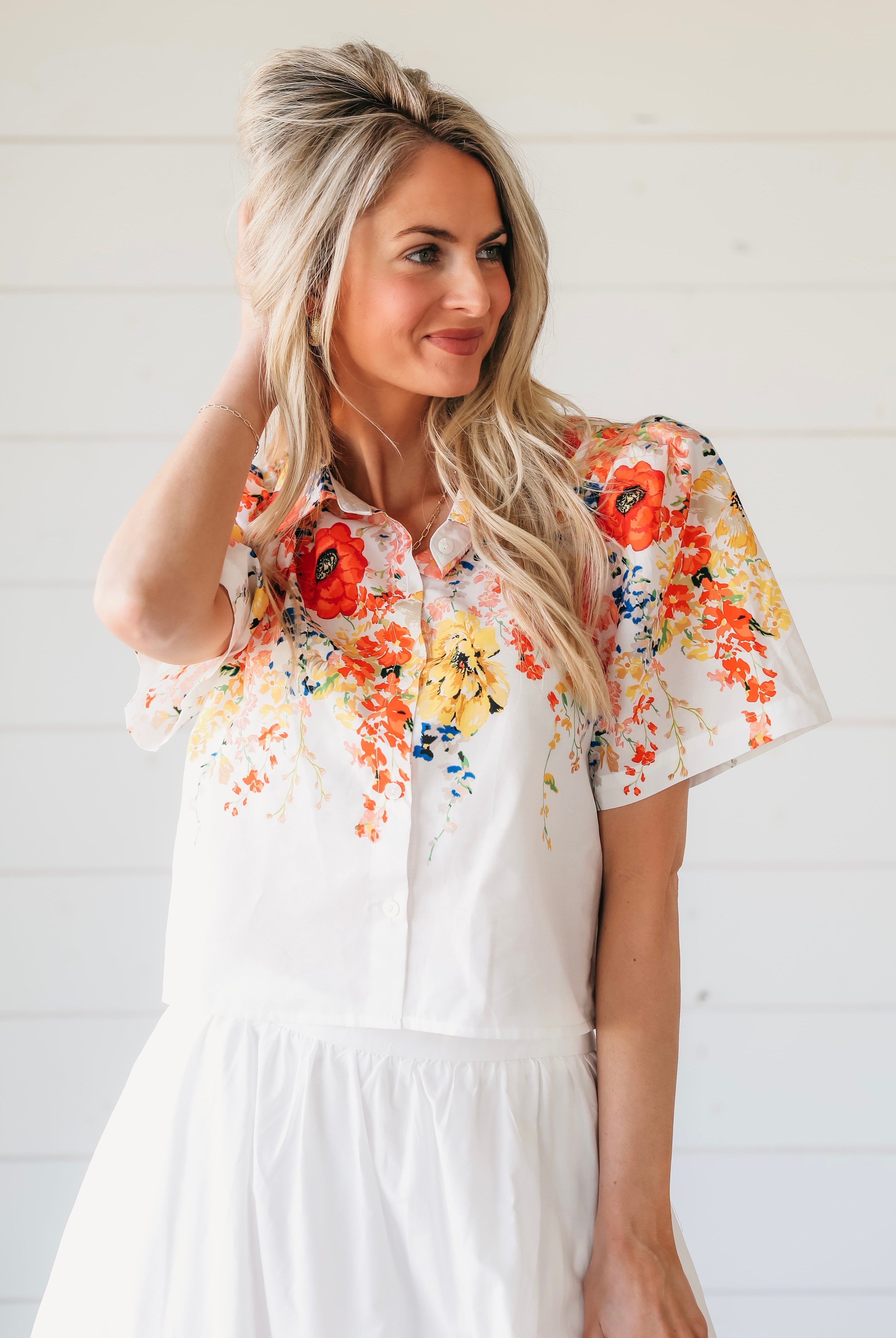 Woman wearing a white two-piece maxi skirt set. The top features a vibrant floral print with red, orange, and yellow