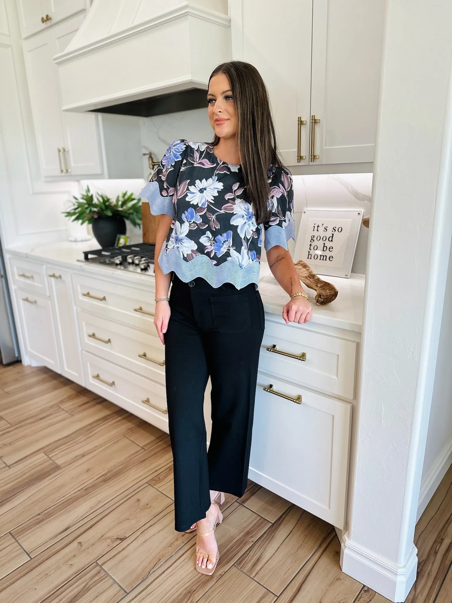 Woman wearing black ponte wide-leg pants and a floral print top, standing in a modern kitchen.