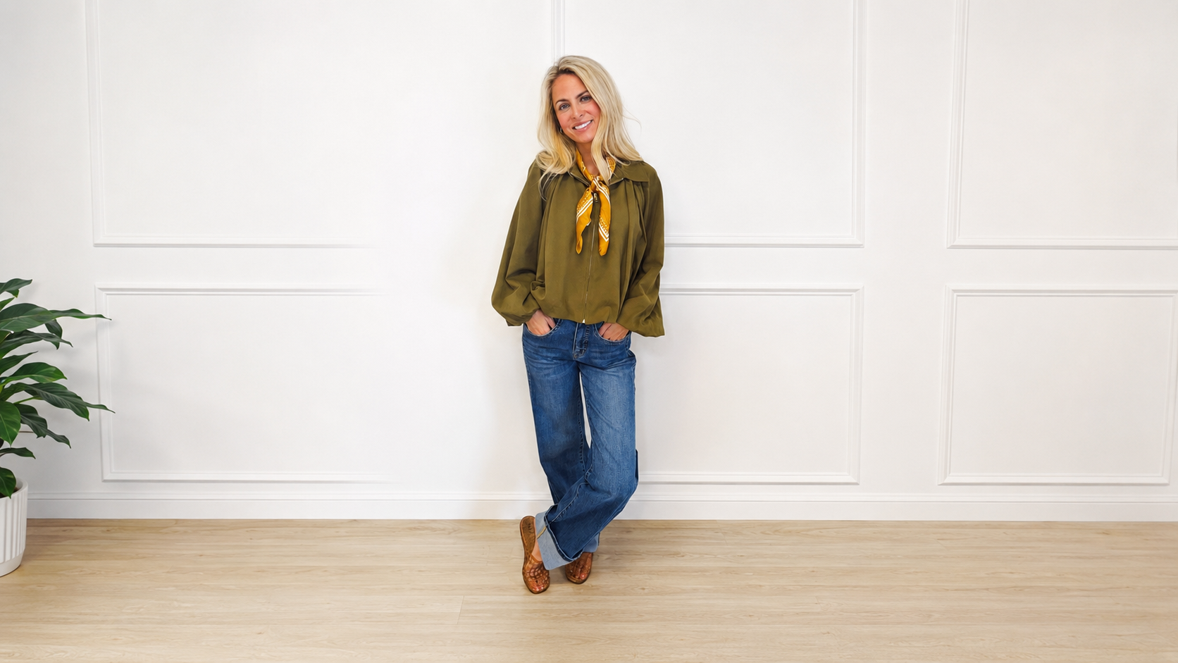 Woman wearing an olive zip-front jacket and cuffed wide-leg denim jeans in a bright white studio