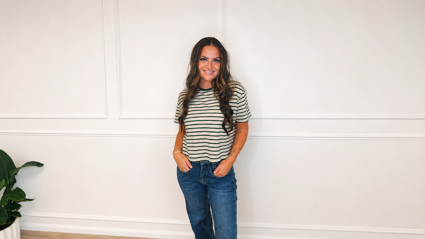 Woman wearing a cream and forest green striped knit tee with medium-wash denim in a bright white studio