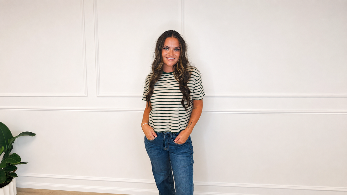 Woman wearing a cream and forest green striped knit tee with medium-wash denim in a bright white studio