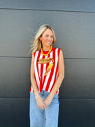 Woman wearing a red and white striped knit tank top with a sequined hot dog graphic, paired with light wash jeans.