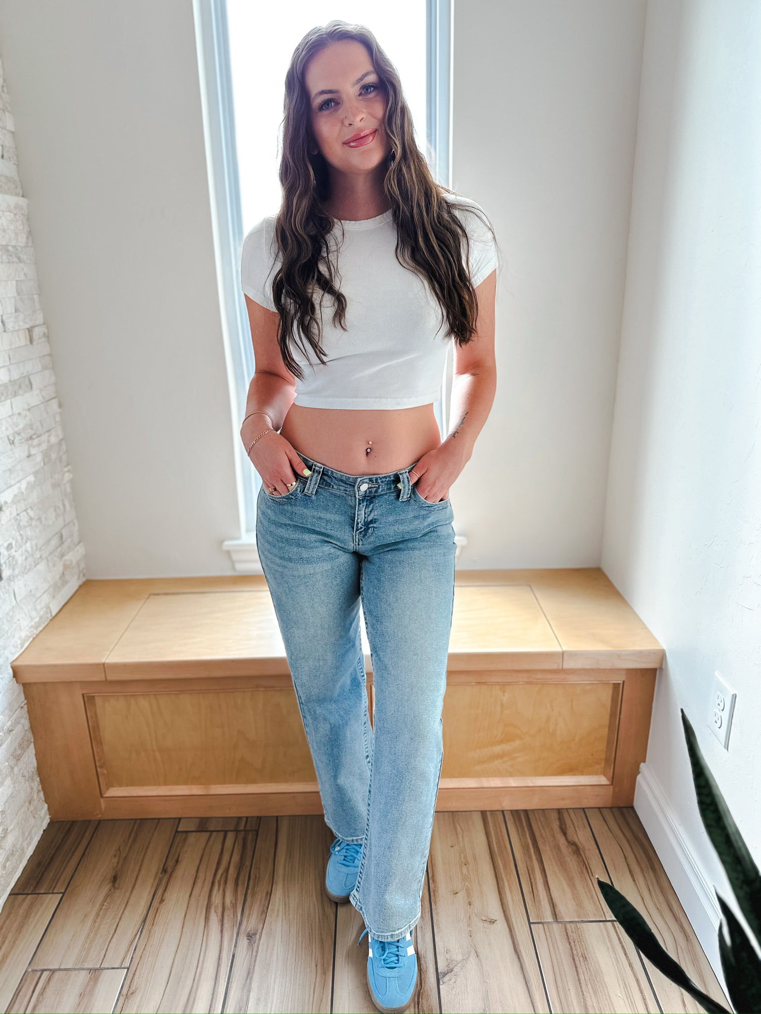 Woman wearing JBD wide leg medium wash low rise denim jeans and white crop top, with blue sneakers. Full body shot.