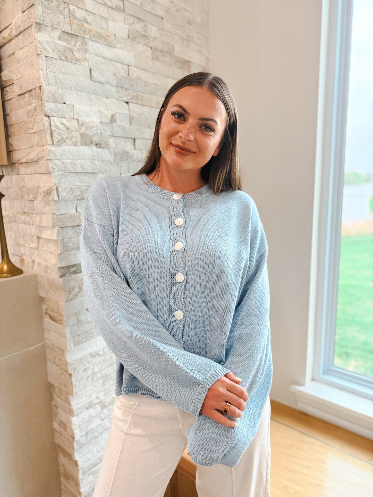 Light blue oversized balloon sleeve cardigan sweater with white buttons. Worn by a woman in white pants.