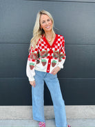 Woman wearing Queen of Sparkles red and white checkered sequin strawberry cardigan with light wash wide-leg jeans.