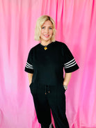 Black and white striped Entro matching set with cropped black top and black sweatpants. Model wears a gold heart necklace.