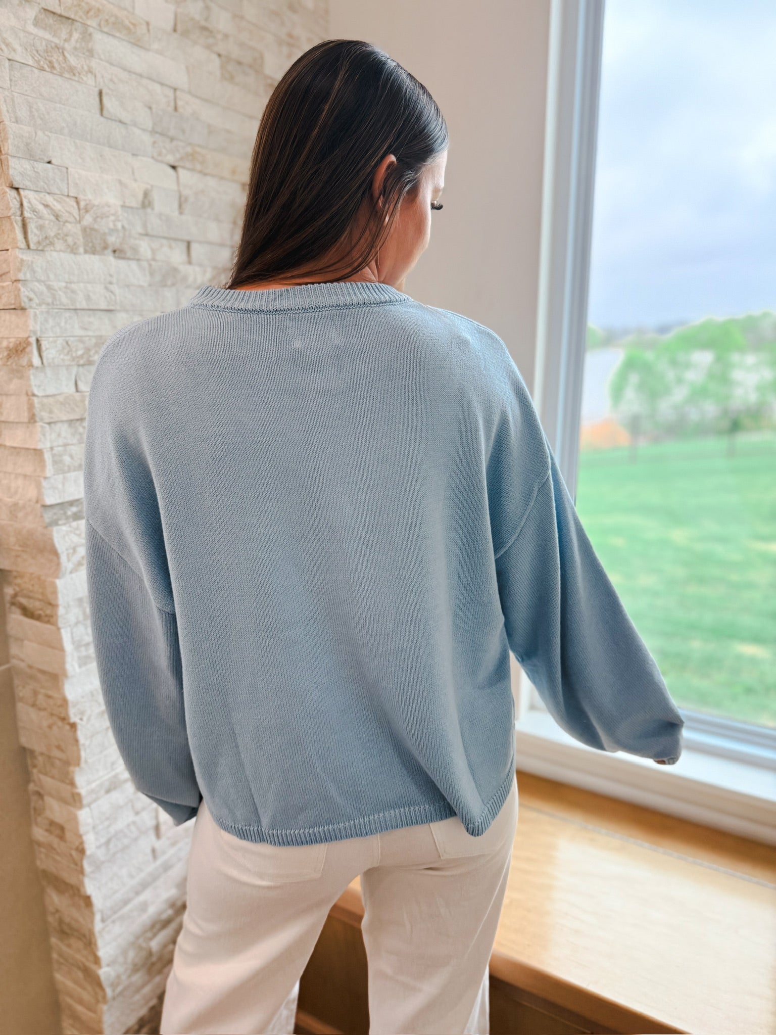 Back view of a woman wearing a light blue oversized cardigan with balloon sleeves and white pants.