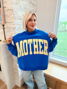 Royal blue mockneck oversized sweatshirt with yellow "MOTHER" graphic print on front. Worn by a blonde woman.