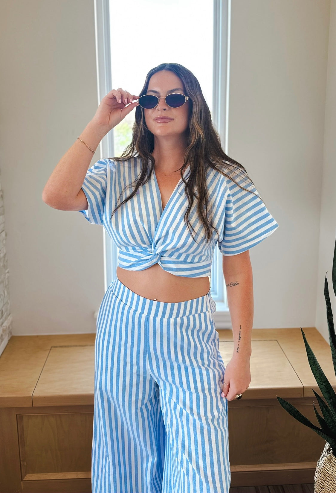 Woman in blue and white striped twist front crop top and wide-leg pants. She wears sunglasses.