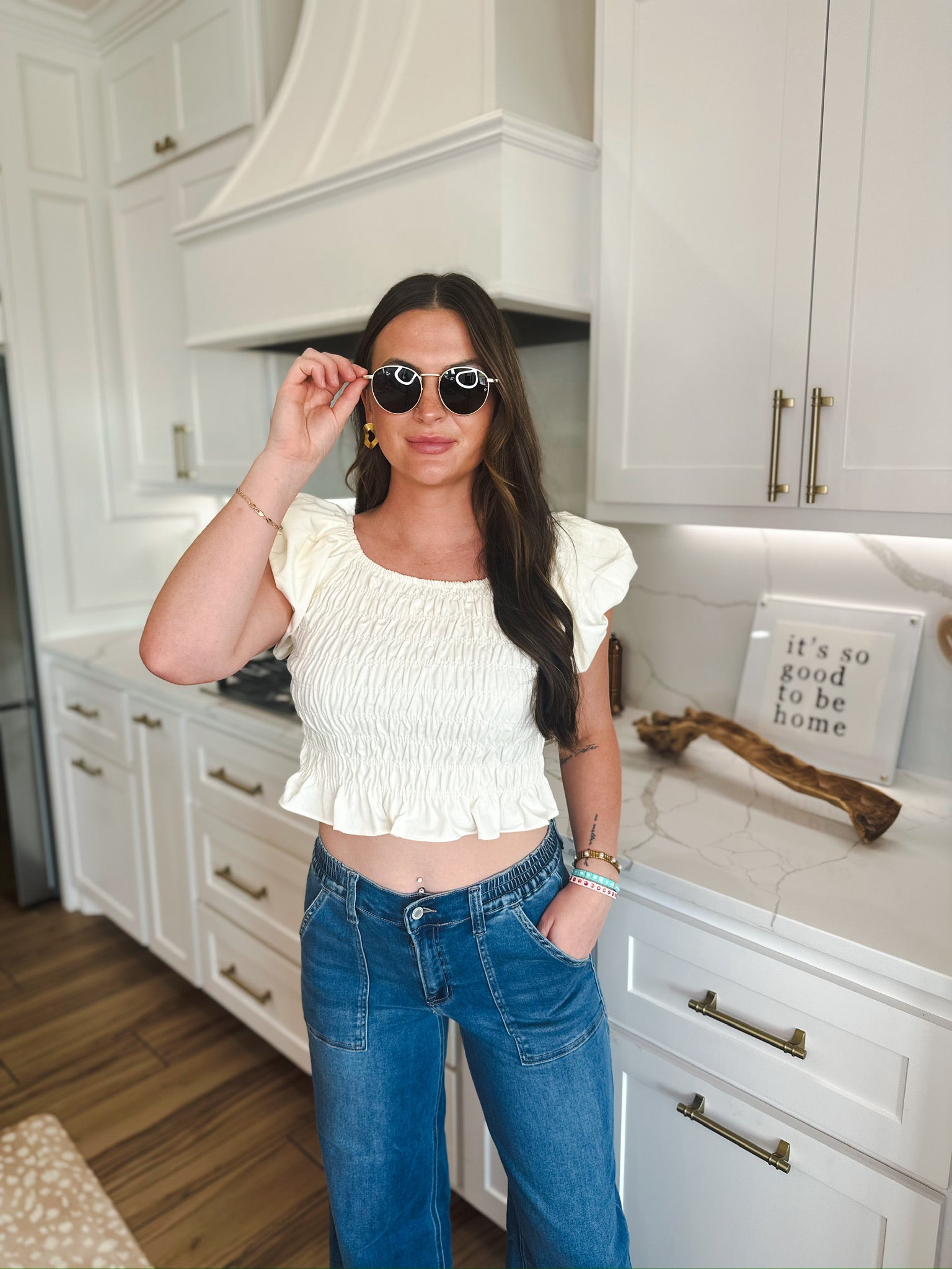 Woman wearing a soft yellow ruched puff sleeve crop top with blue denim jeans, accessorized with sunglasses and bracelets.