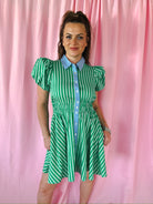 A woman wears a green and white striped dress with blue contrast collar and puff sleeves. The dress has a cinched waist and