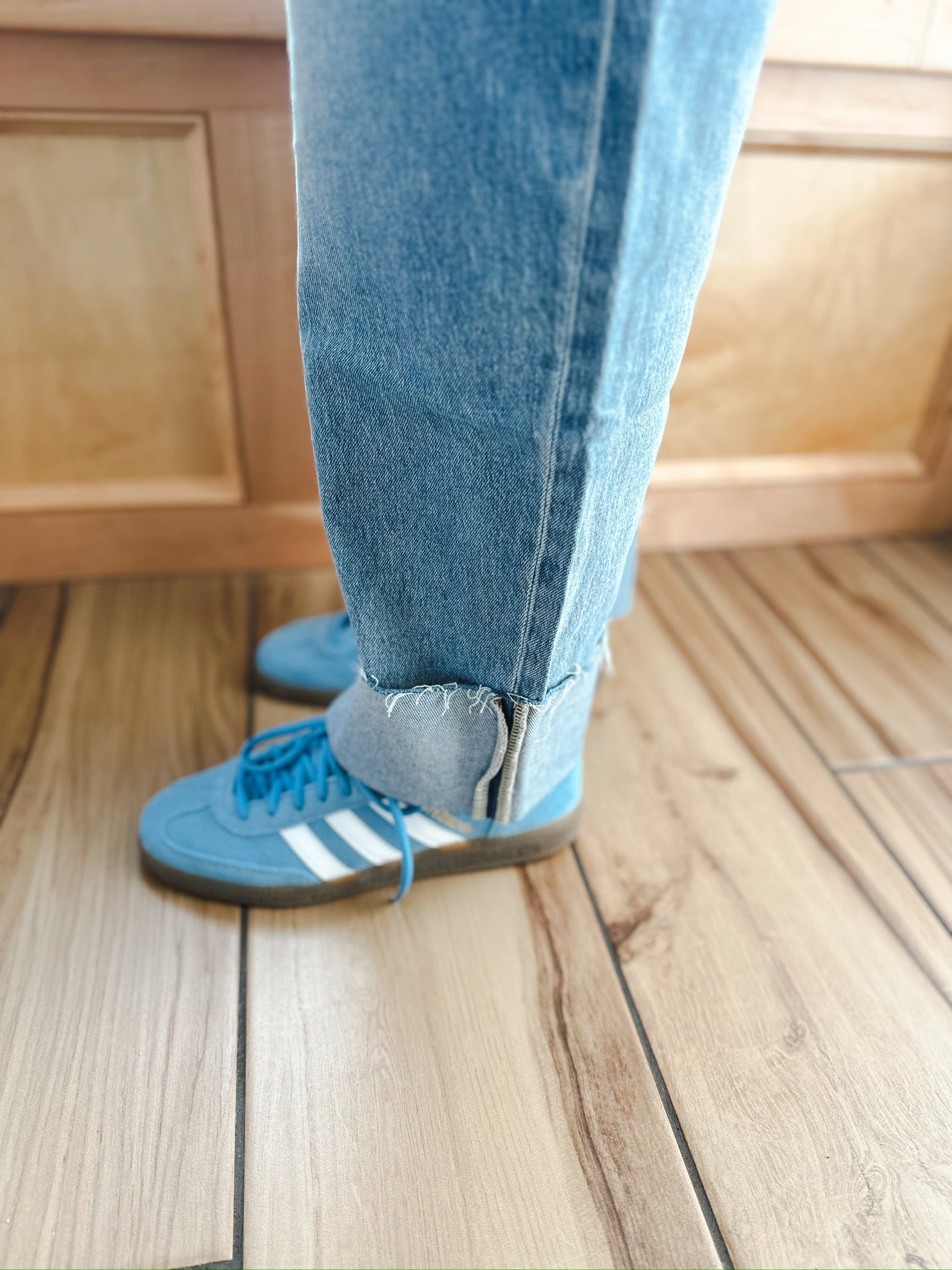 Light wash MICA barrel jeans with cuffed raw hems worn with blue Adidas sneakers.