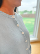 Light blue knit cardigan with white buttons down the front. Close-up view of the neckline and chest area.