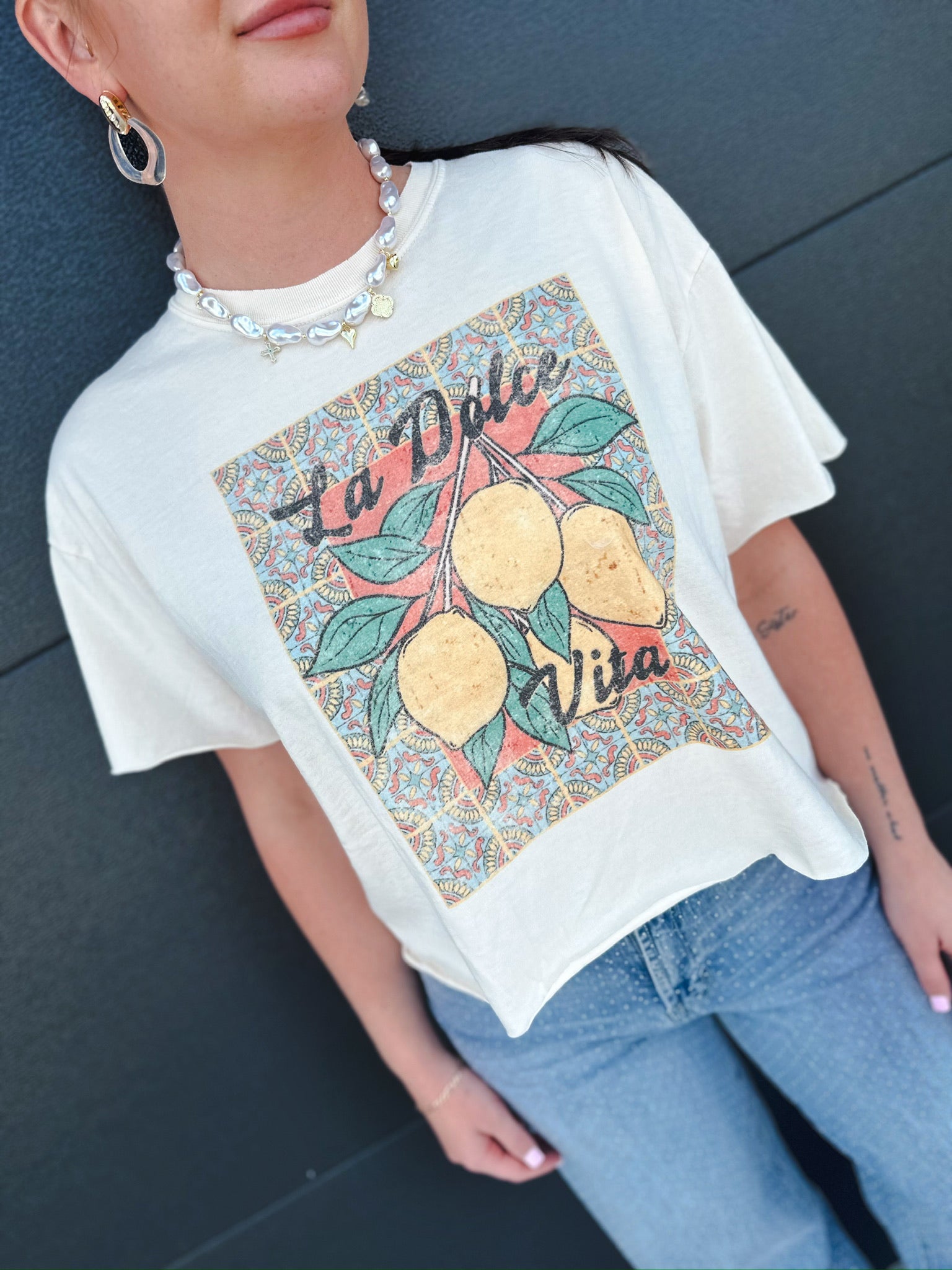 Cream La Dolce Vita vintage crop tee with a graphic of lemons on a branch against a colorful patterned background.