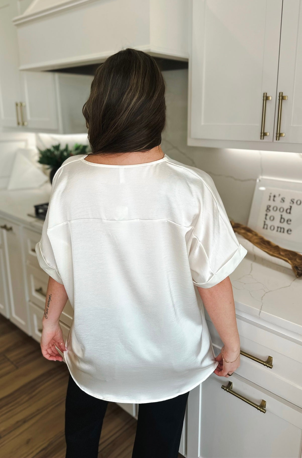 Back view of a woman wearing an ivory satin V-neck high-low blouse with cuffed short sleeves.