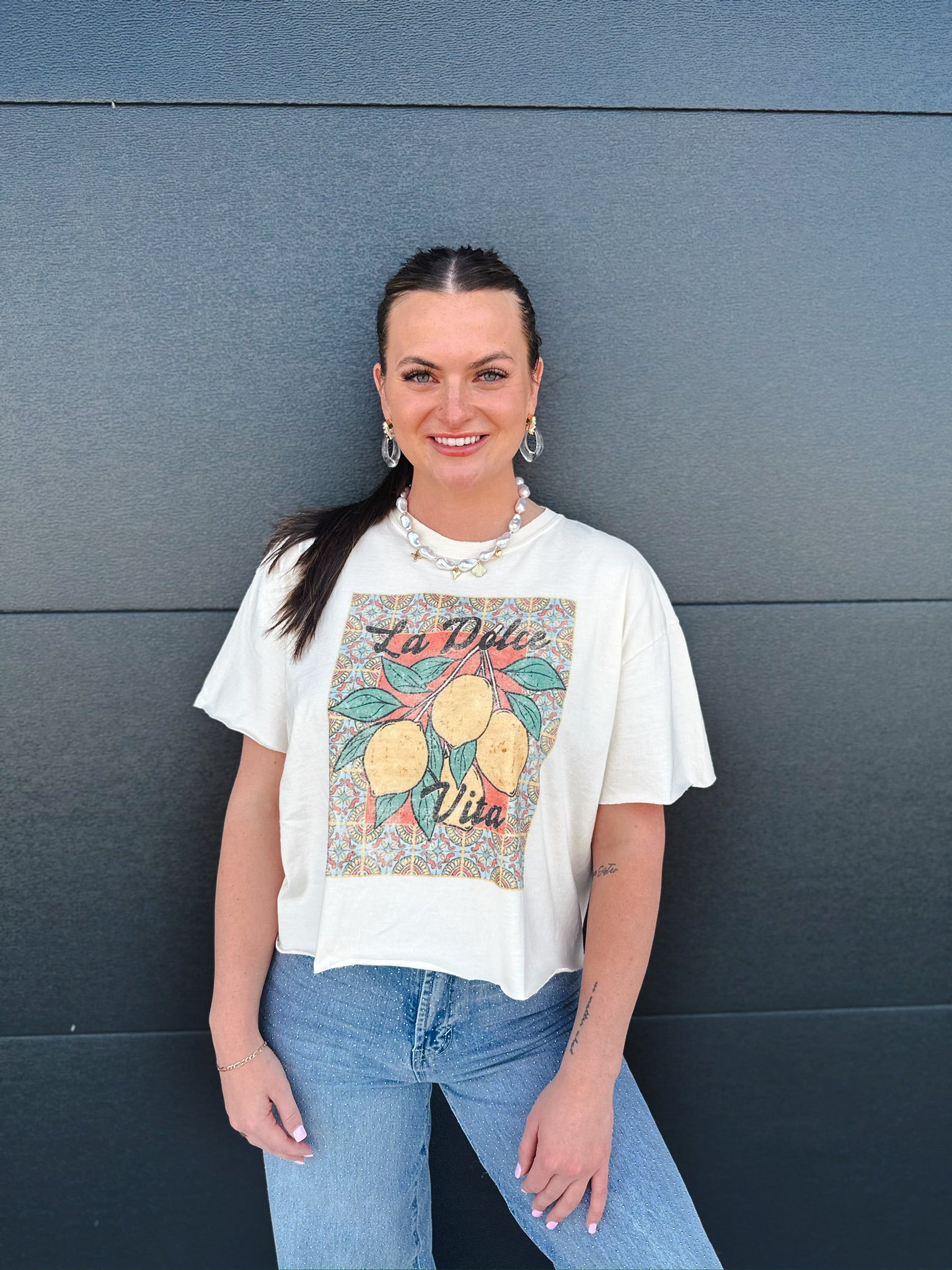 Cream La Dolce Vita vintage graphic crop tee with a lemon branch design and patterned background.