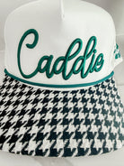 White caddie hat with green "Caddie" embroidery and black and white houndstooth brim.