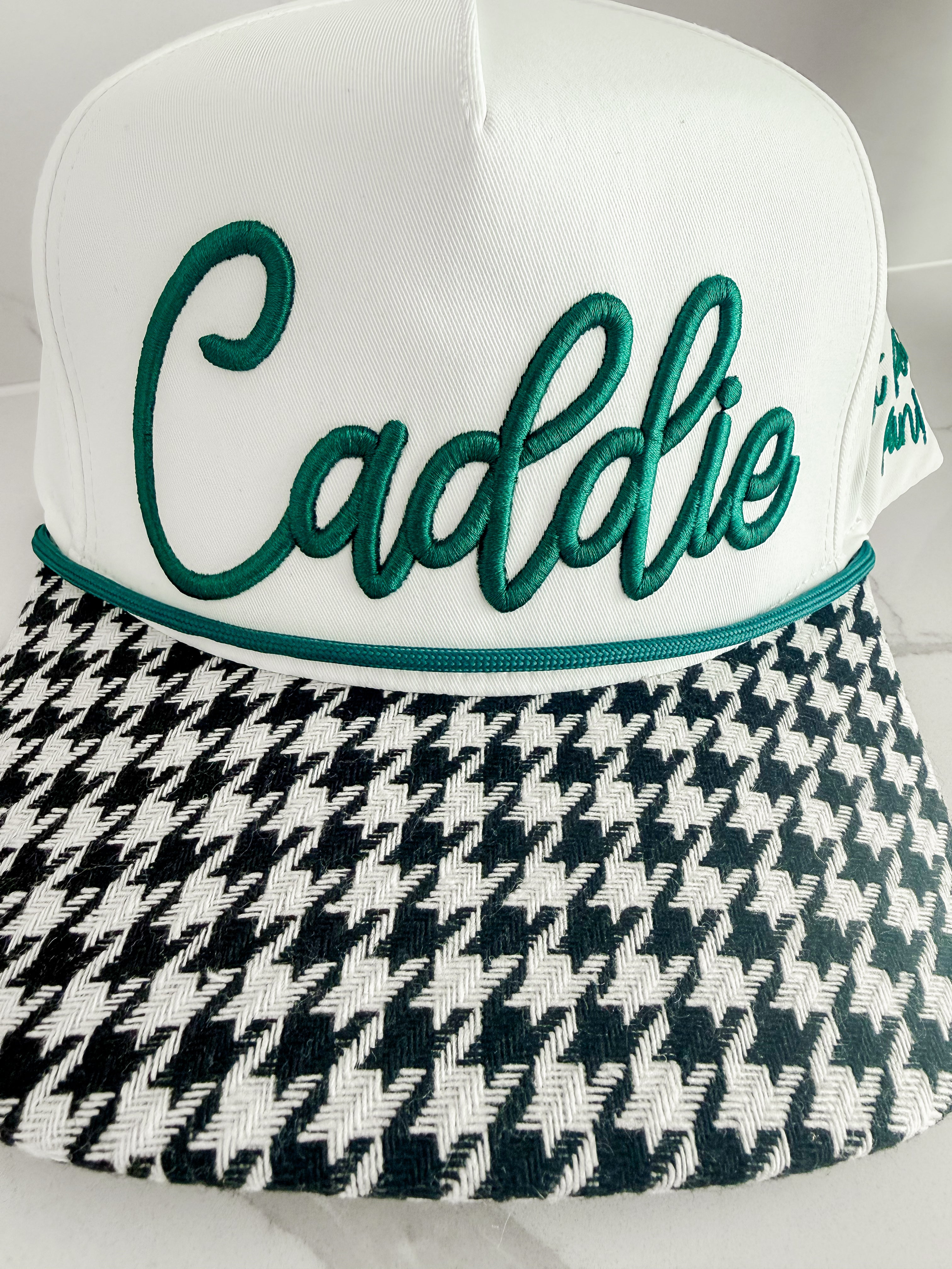 White caddie hat with green "Caddie" embroidery and black and white houndstooth brim.