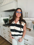 Woman wearing a black and cream striped knit sweater vest with v-neck and button detail, paired with textured silver pants.