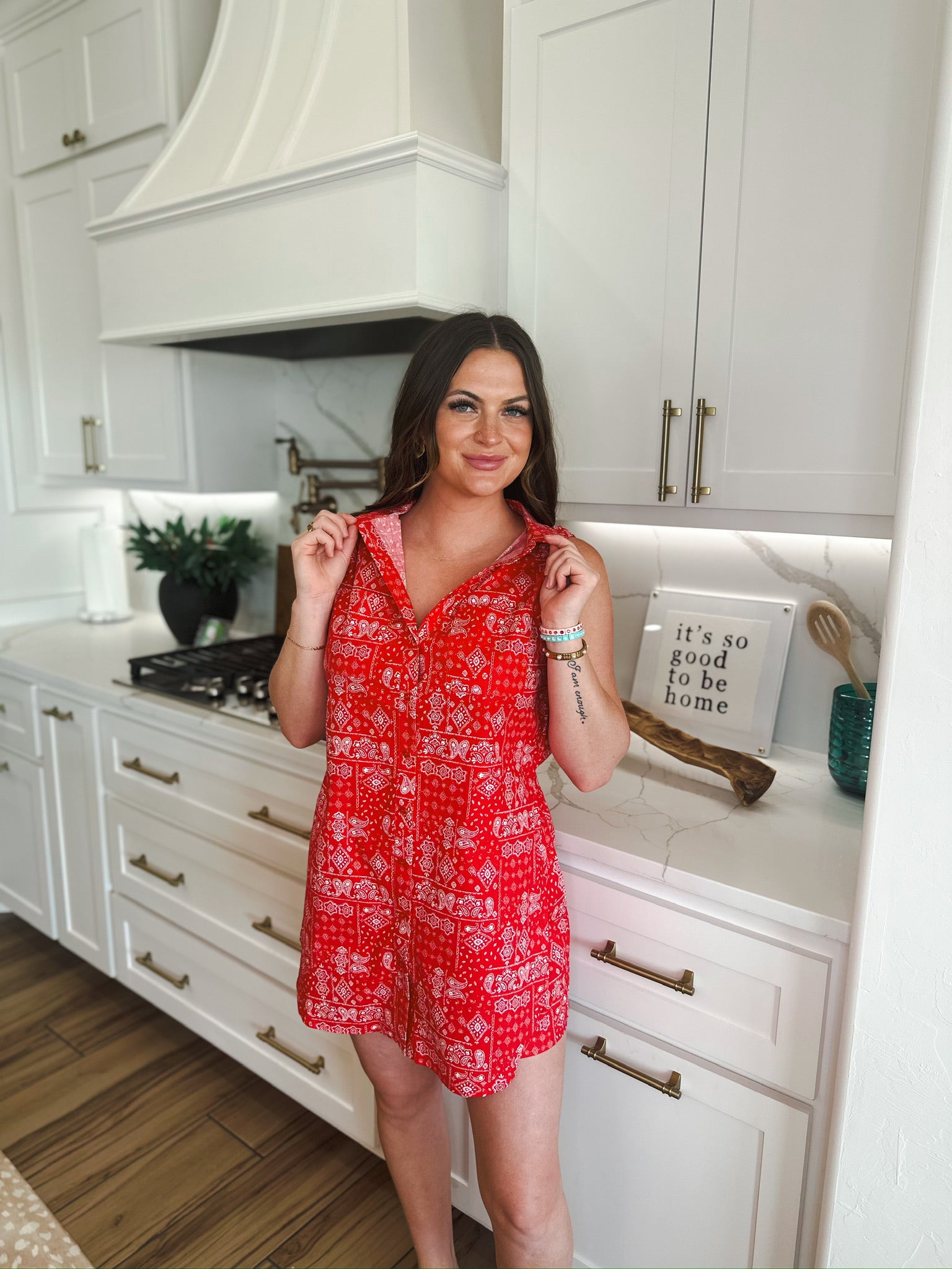 Red sleeveless romper with a white bandana print. A woman stands in a kitchen wearing the romper.