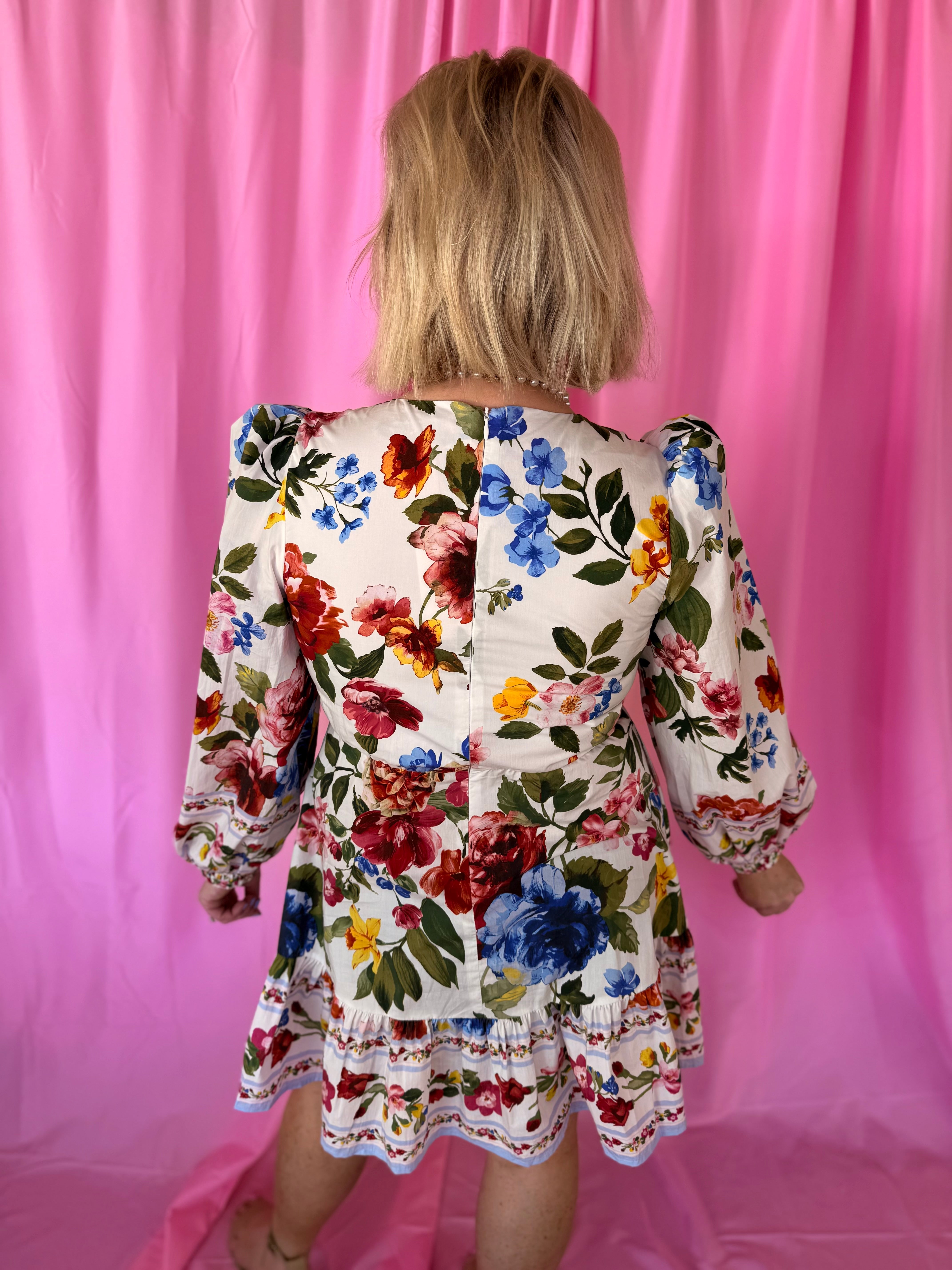 Back view of a white floral puff sleeve mini dress with red, blue, pink, yellow flowers and green leaves. Features a