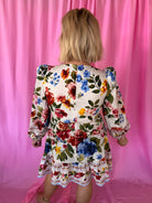 Back view of a white floral puff sleeve mini dress with red, blue, pink, yellow flowers and green leaves. Features a