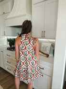 Woman from behind wearing a red and cream floral halter mini dress with a tie neck and ruffled hem.