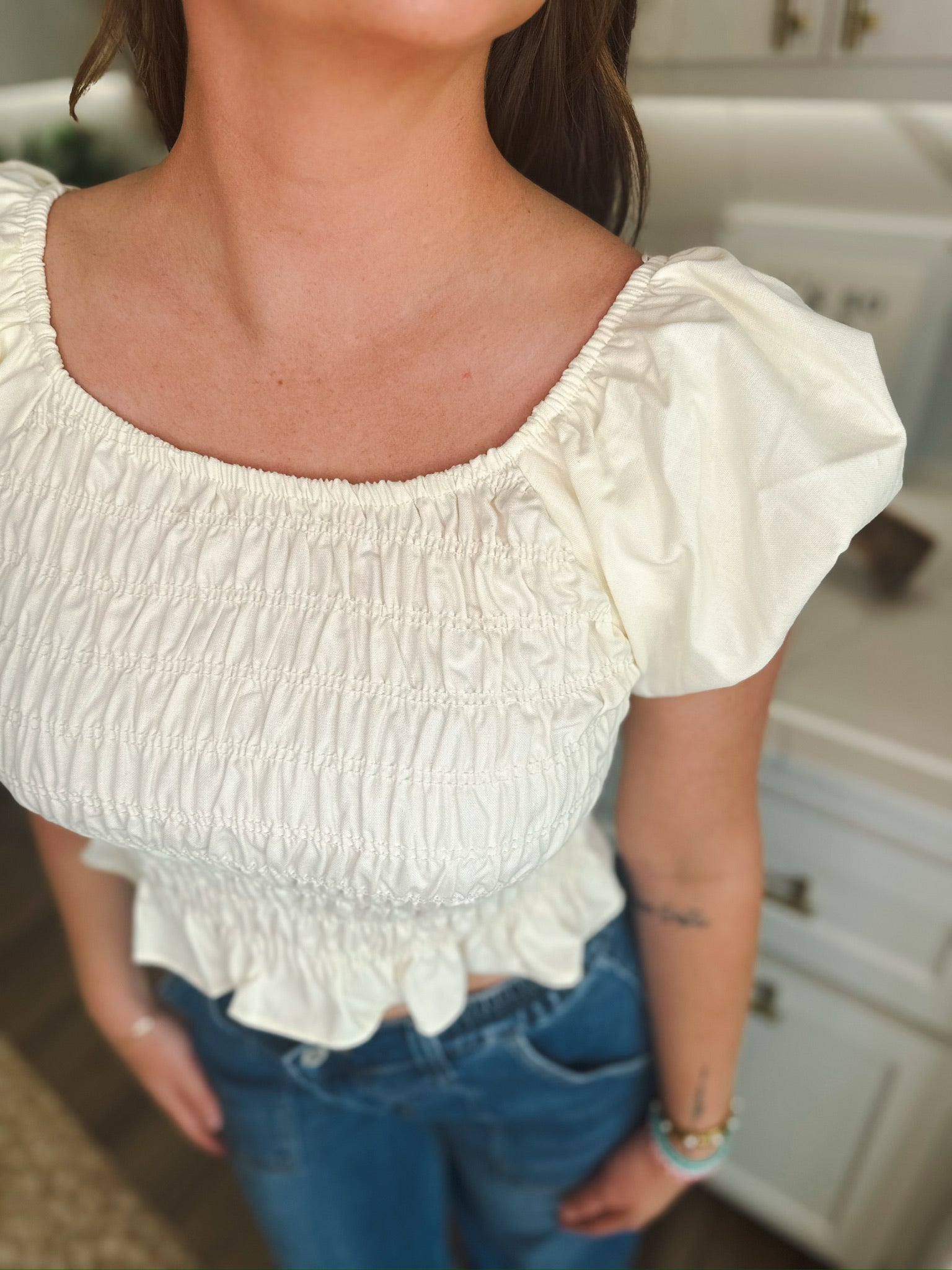 Cream puff sleeve ruched blouse with a square neckline, cinched waist, and ruffled hem, worn with blue jeans.
