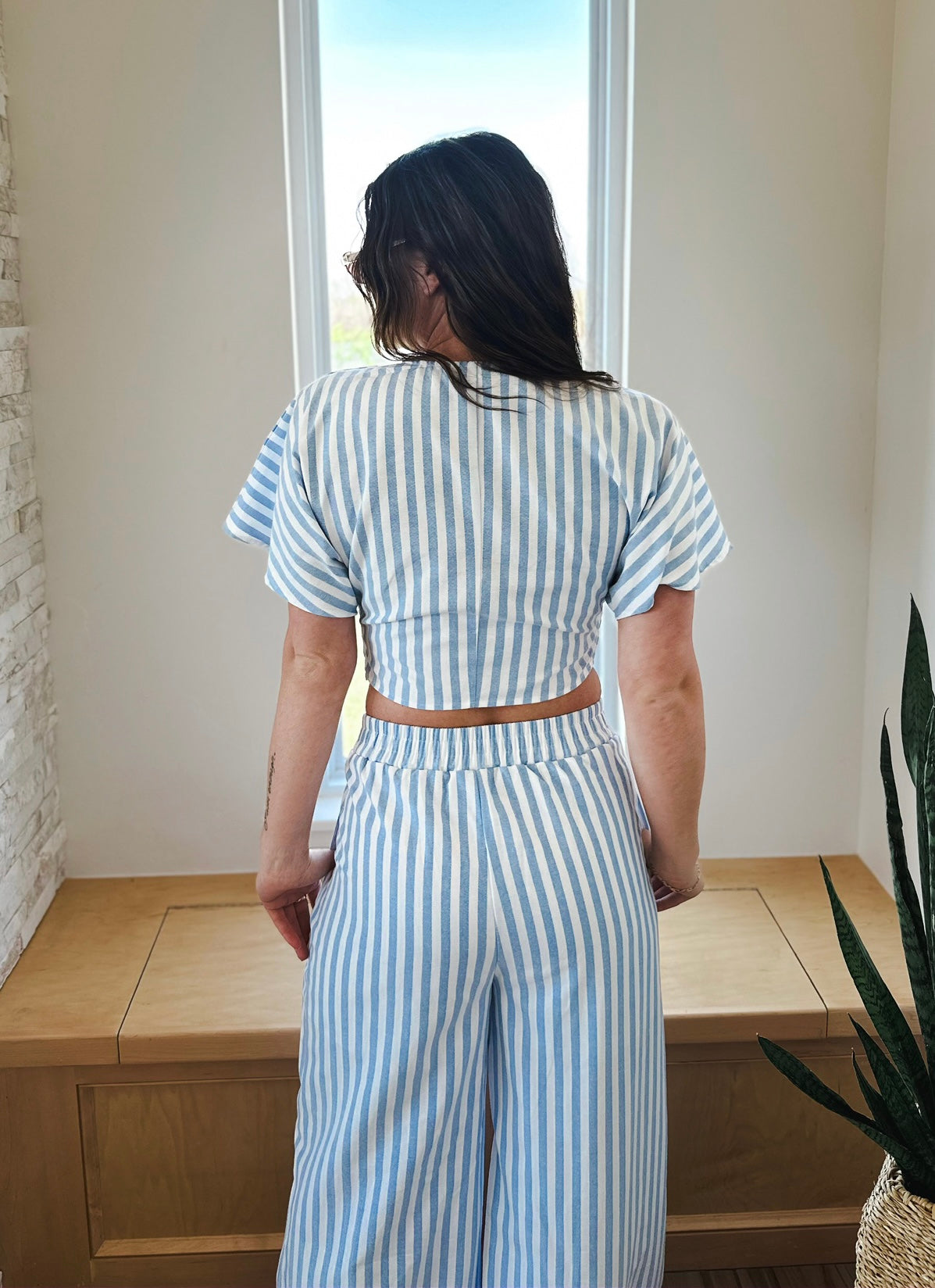 Back view of a woman wearing a blue and white striped twist front crop top and matching wide-leg pants set.