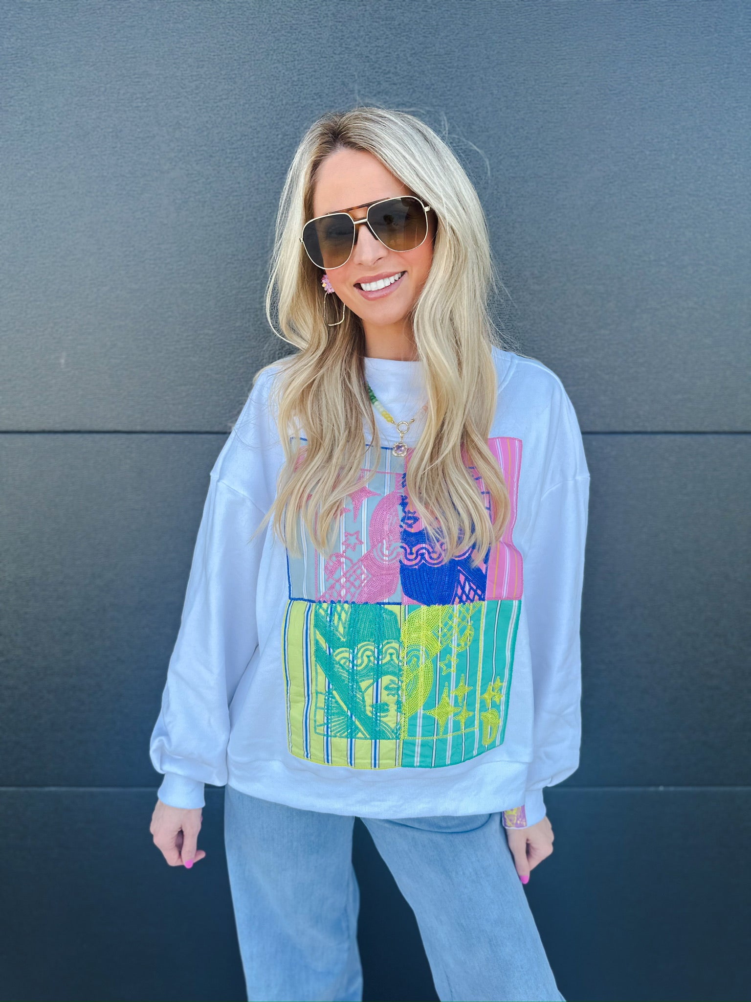 White Queen of Sparkles sweatshirt with colorful abstract graphic print and mock neck. Woman wearing sunglasses and jeans.
