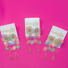 Spring floral dangle earrings with pastel colored flowers and leaf charms on white display cards.