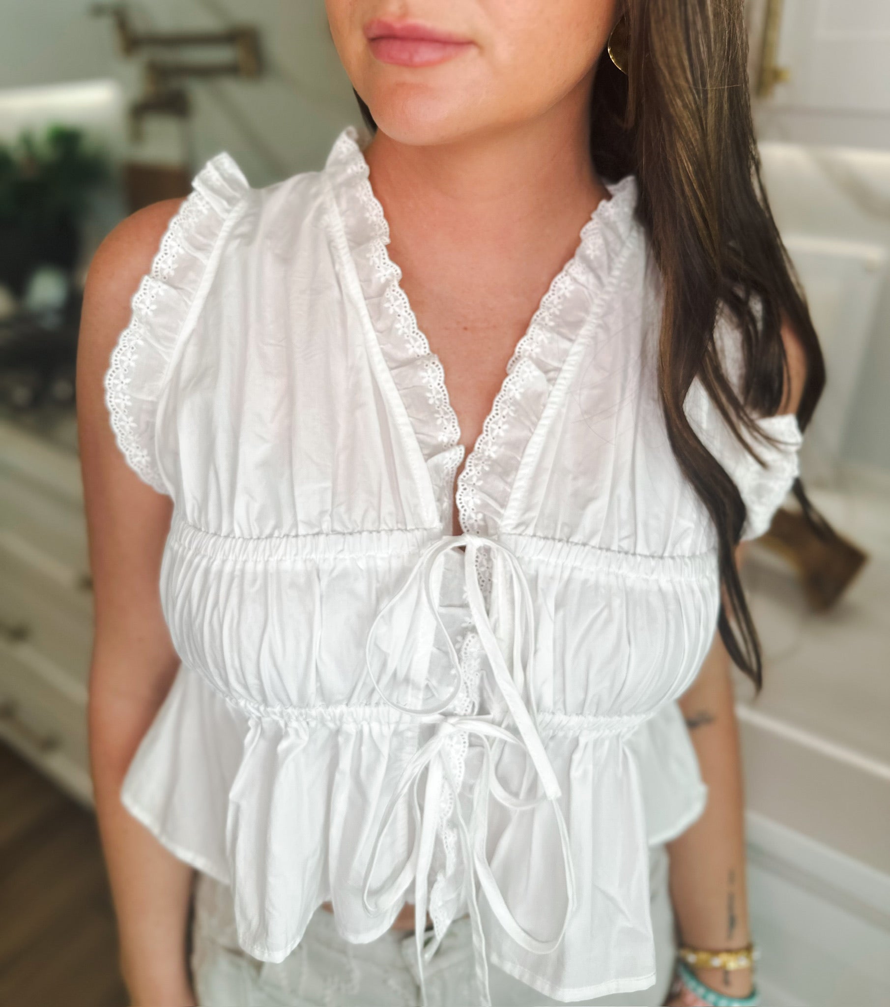 Woman wearing a white lace trim tie-front peplum top with ruffled short sleeves and a V-neckline.
