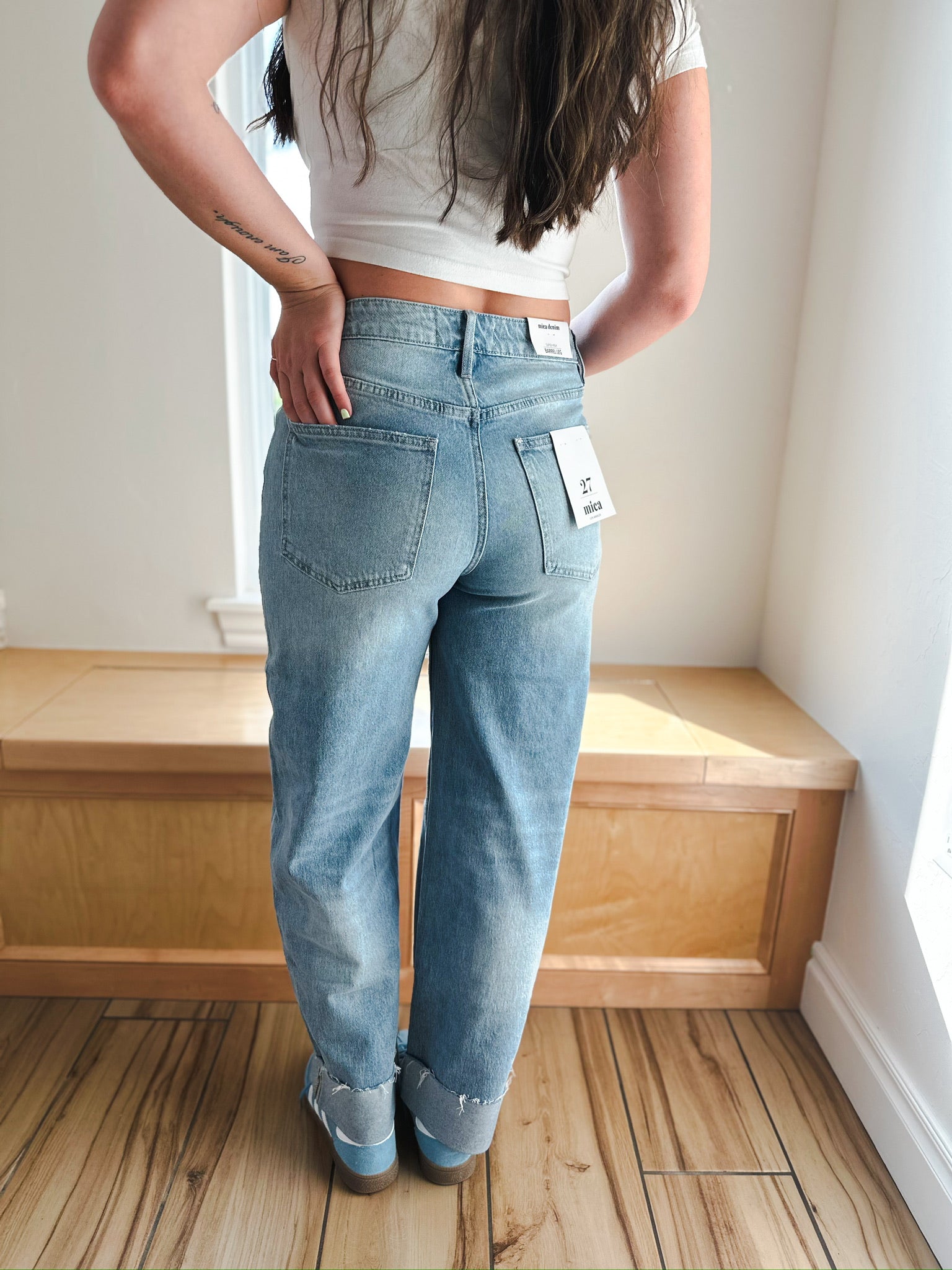 MICA LIGHT WASH CUFFED BARREL JEANS: A woman stands facing away, wearing light wash barrel jeans with cuffed, frayed hems