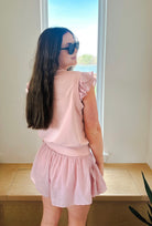 Woman wearing a light pink athleisure set: a sleeveless pullover with ruffle sleeves and crinkle nylon shorts.