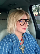 Woman wearing oversized tortoise shell bluelight glasses and a blue striped shirt with a colorful beaded necklace featuring