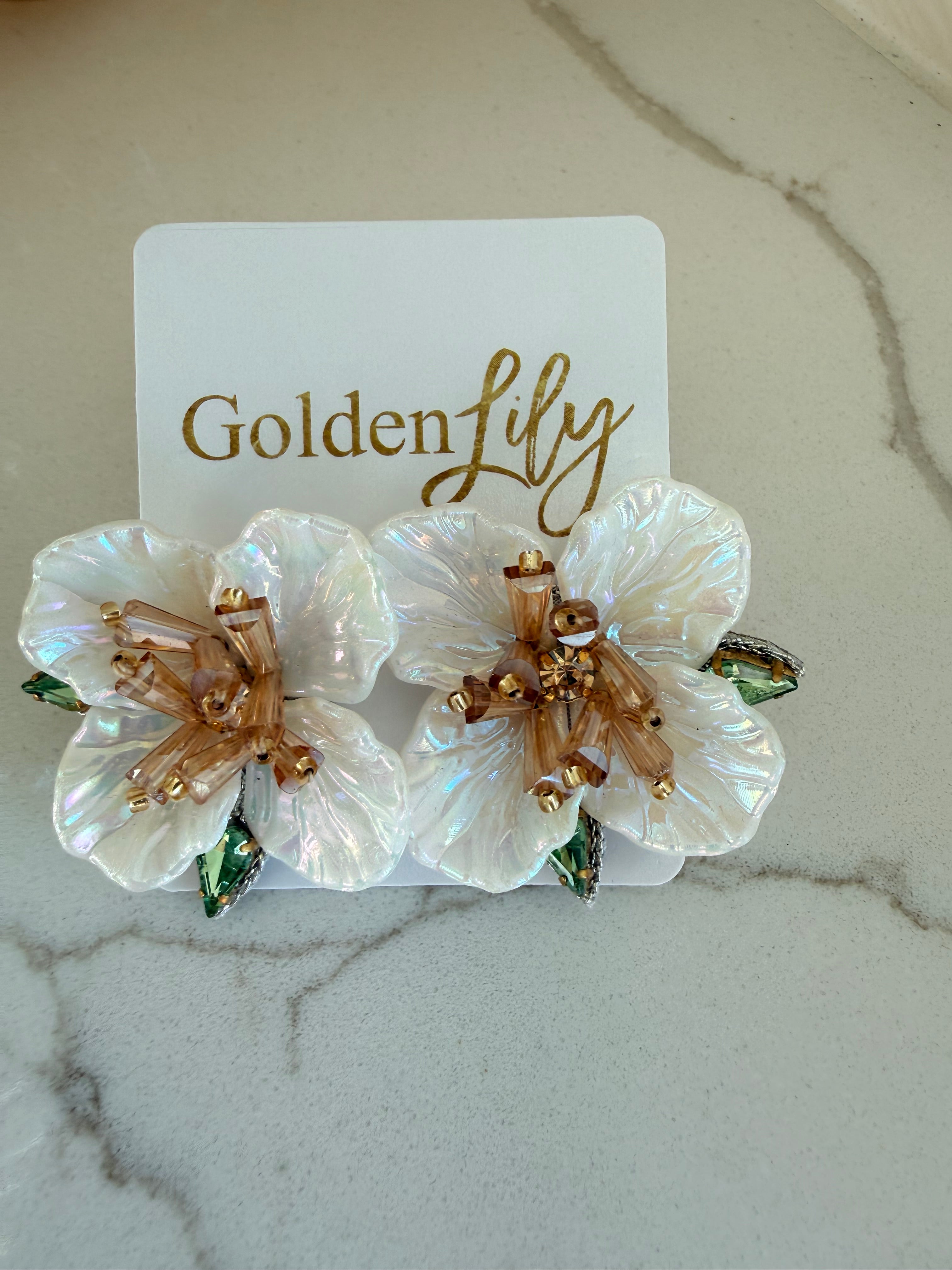 Large white iridescent floral stud earrings with amber beads and green gem accents on a white card.
