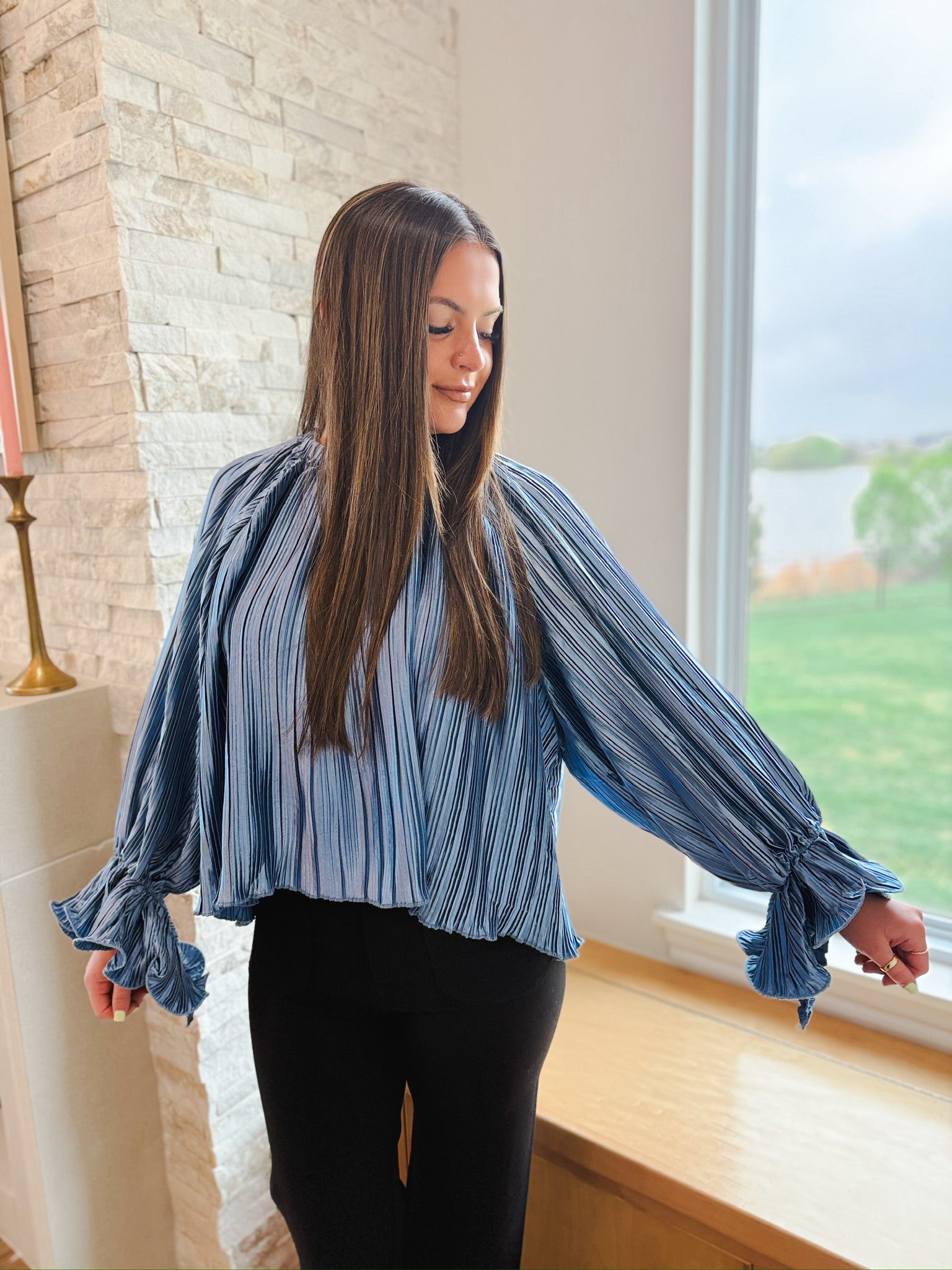 Slate blue pleated long sleeve top with ruffle cuffs, worn by a woman.