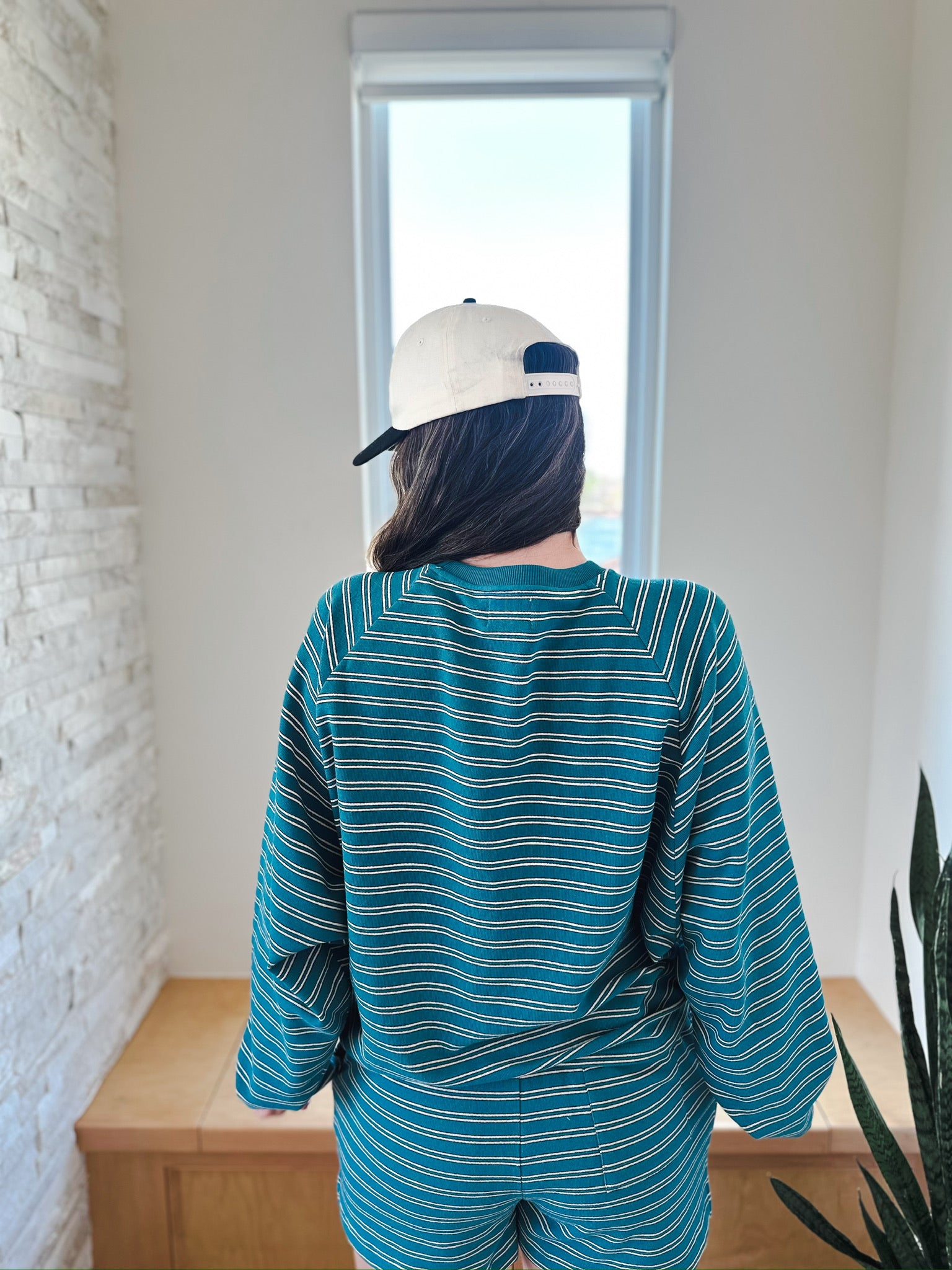 Teal and white striped long sleeve top and elastic waist shorts set worn by a person facing away, wearing a cream baseball