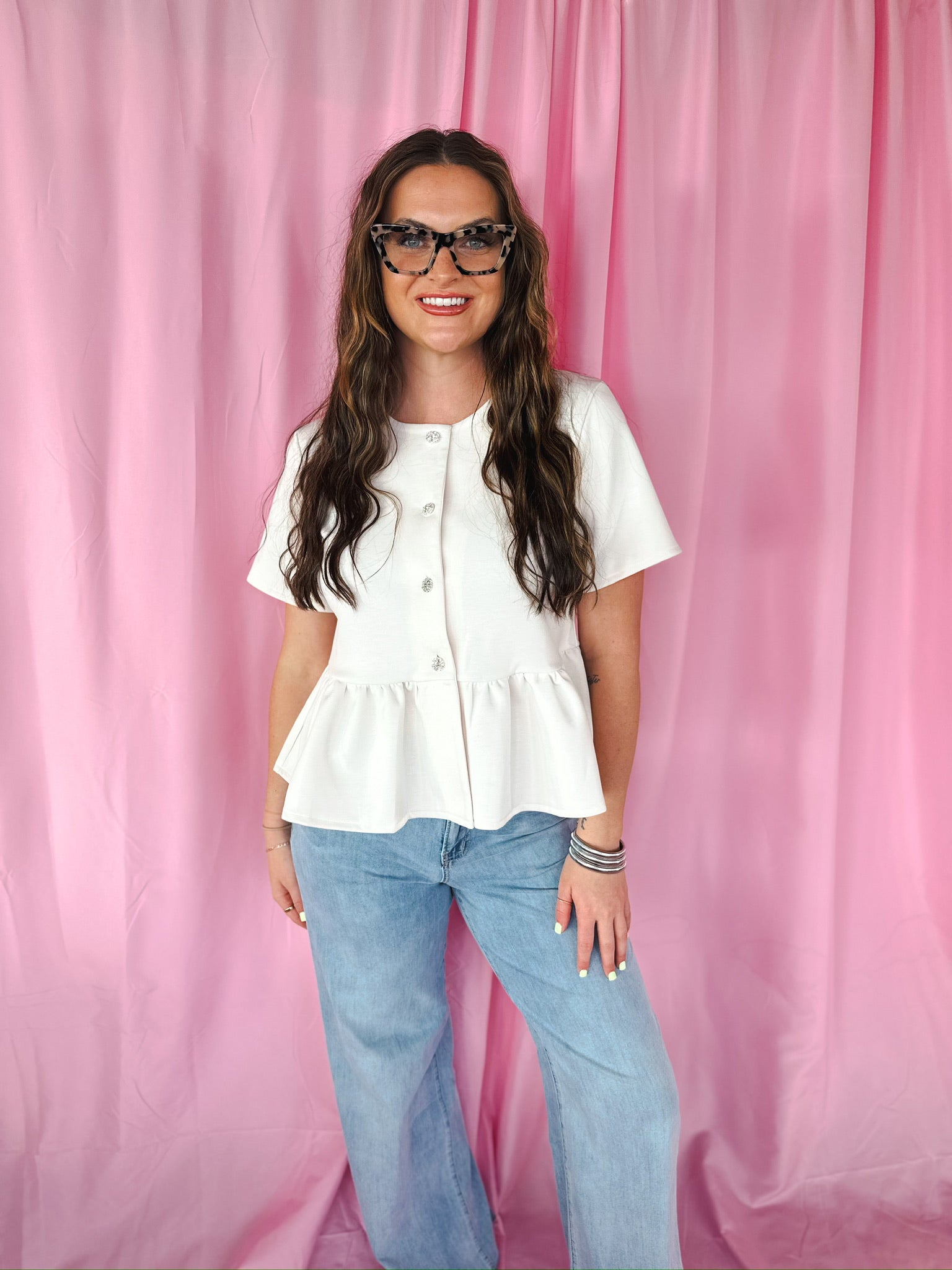 Entro cream peplum jacket with jeweled buttons and short sleeves worn by a woman with glasses and light wash jeans.