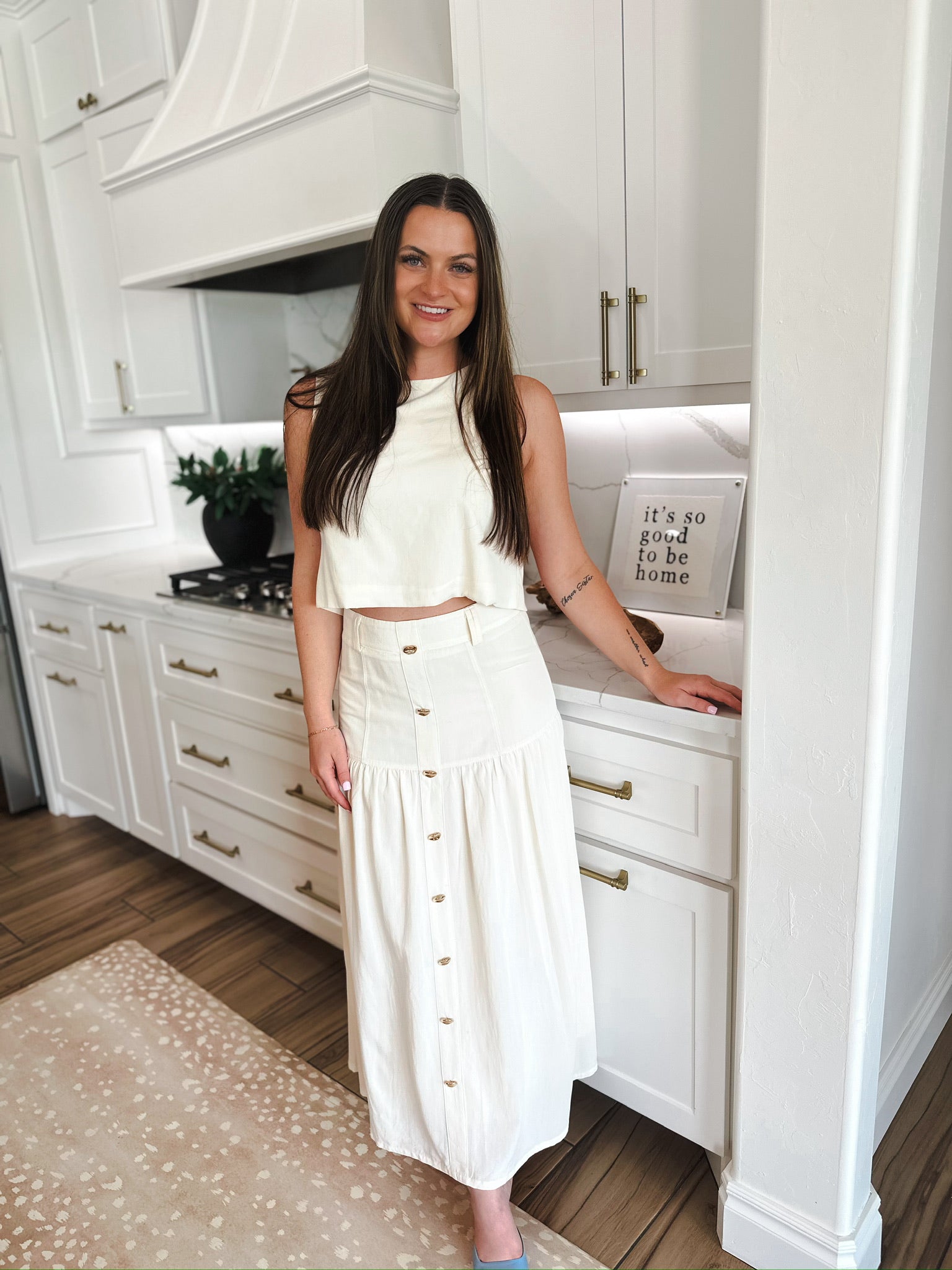 Woman wearing an elegant cream matching set: a cropped sleeveless top and a button-front midi skirt, standing in a modern
