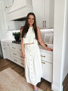 Woman wearing an elegant cream matching set: a cropped sleeveless top and a button-front midi skirt, standing in a modern