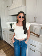 Woman wearing a soft yellow puff sleeve ruched blouse with a square neckline and a ruffled hem, paired with blue denim