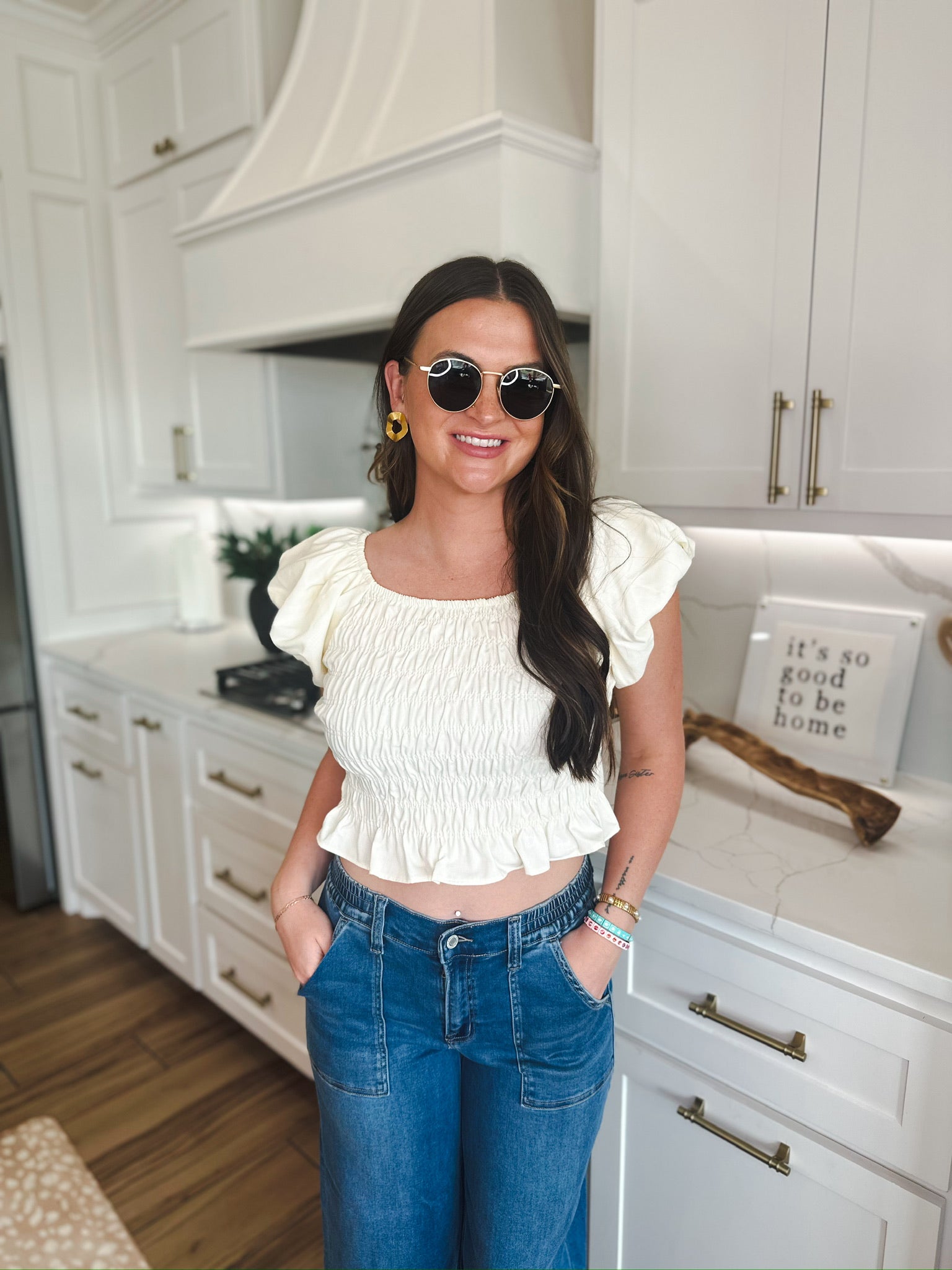 Woman wearing a soft yellow puff sleeve ruched blouse with a square neckline and a ruffled hem, paired with blue denim
