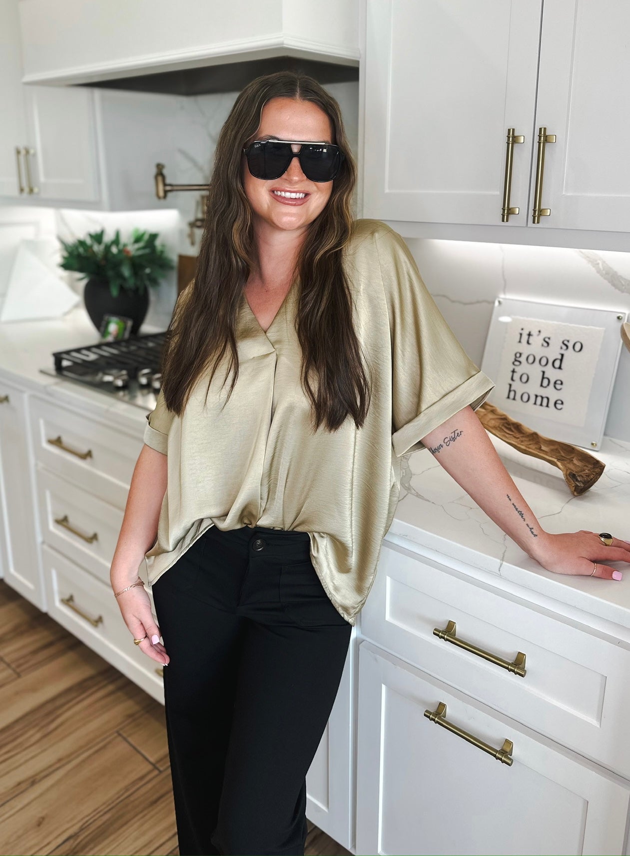 Woman in taupe satin V-neck blouse and black pants, wearing sunglasses.