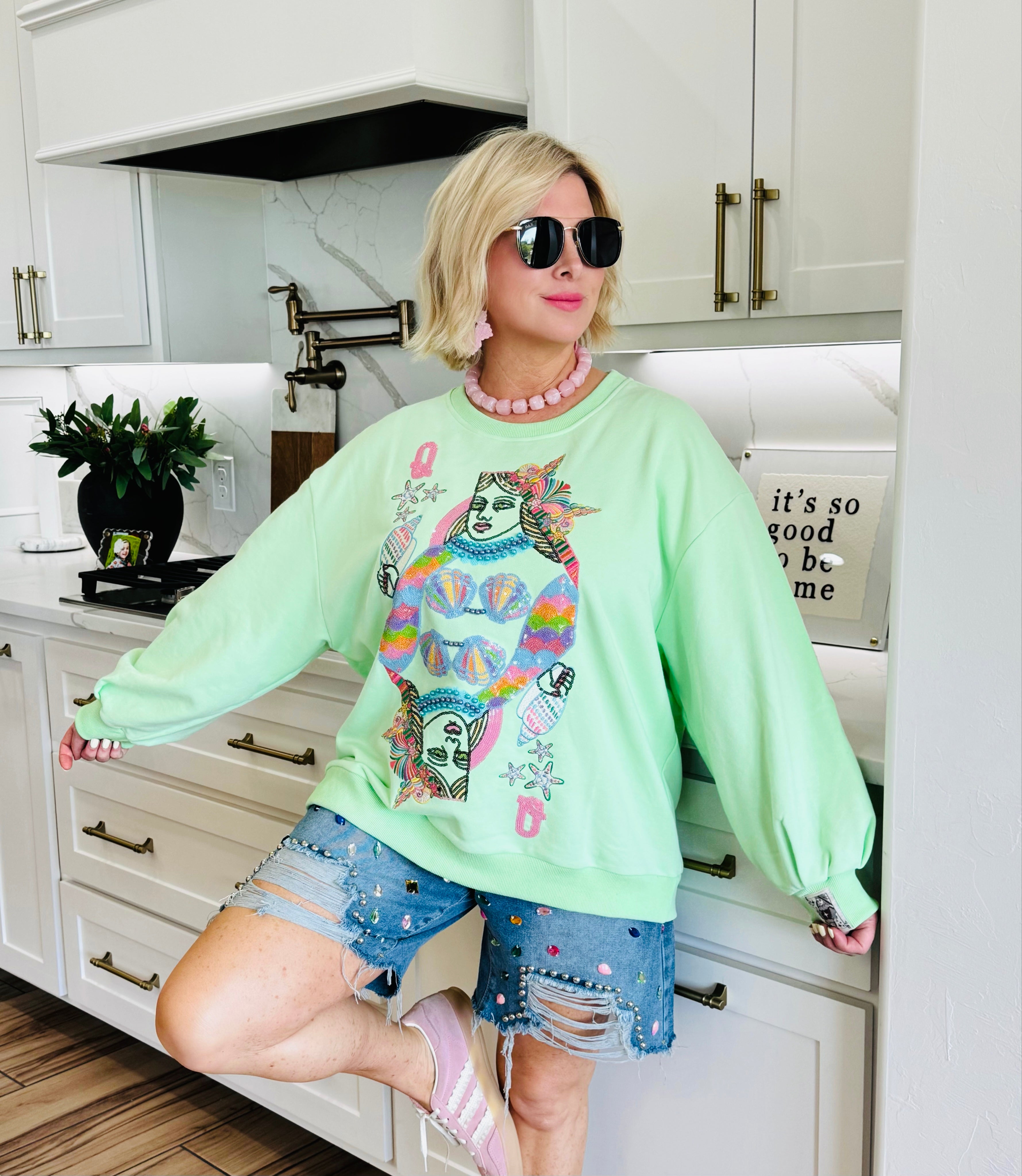 Light green sweatshirt featuring a Queen of the Sea card graphic with mermaid imagery. The graphic has rainbow colors and