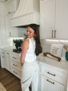 Woman in a white lace trim tie-front peplum top and light-wash patterned pants, standing in a modern white kitchen.