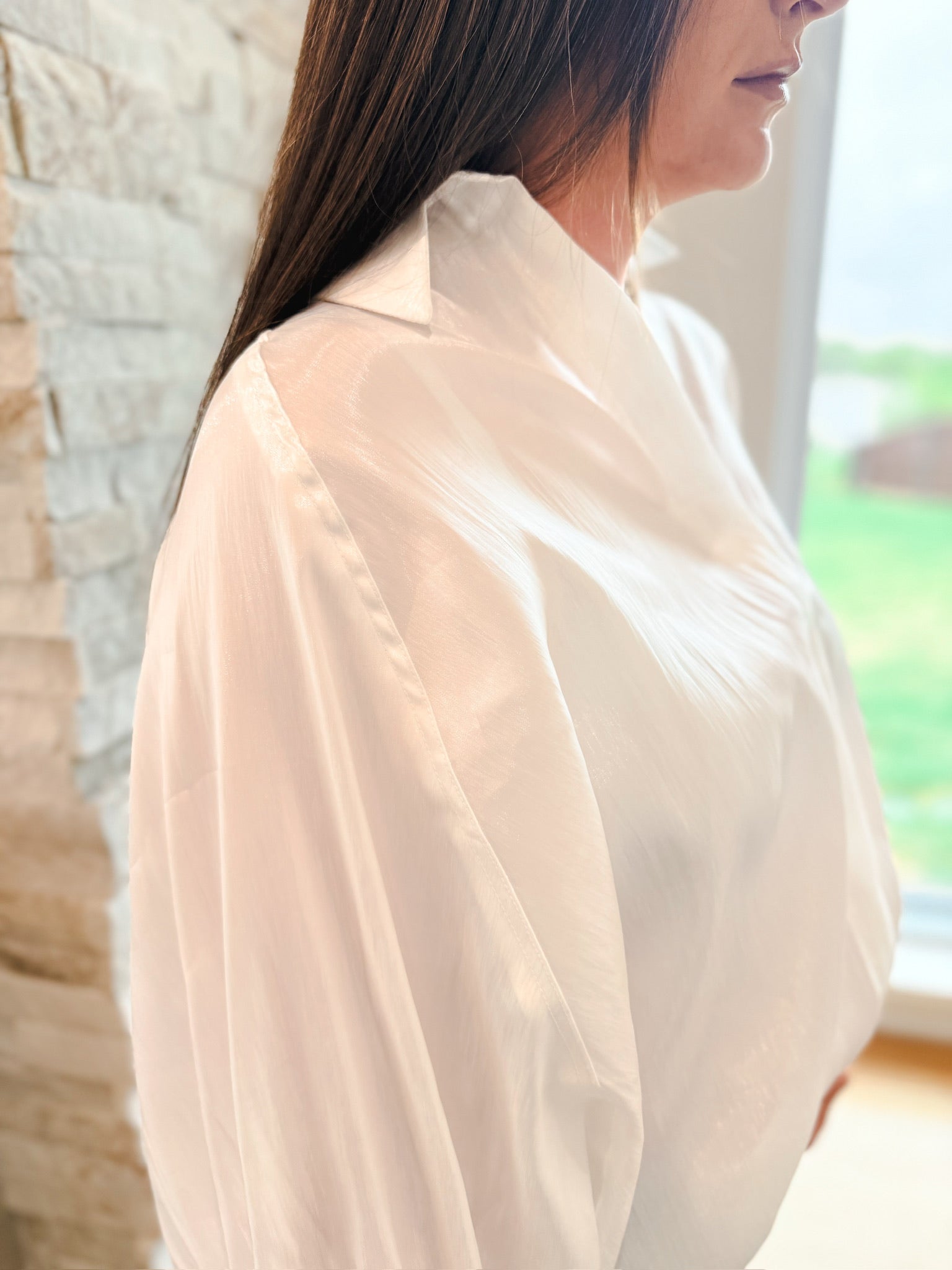 White shiny button front blouse with wide sleeves and a raised collar, showcasing its elegant flowy fabric.