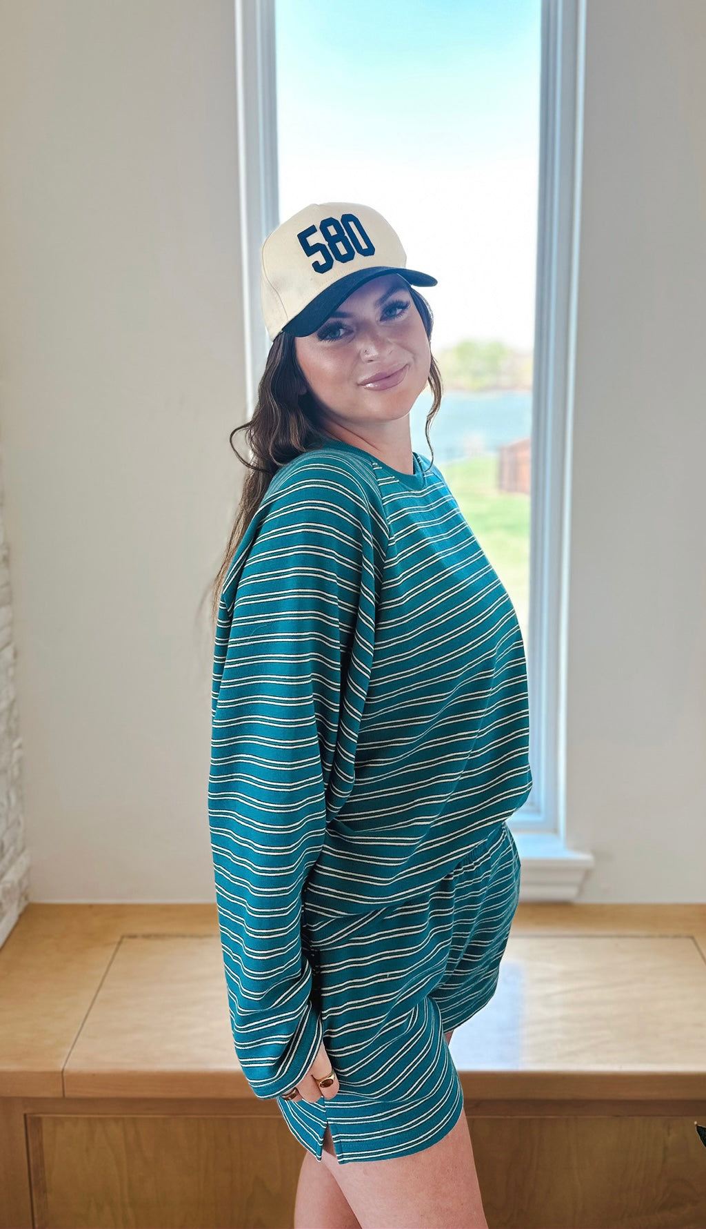 Woman wearing a teal and white striped long sleeve top and matching shorts, with a '580' baseball cap.