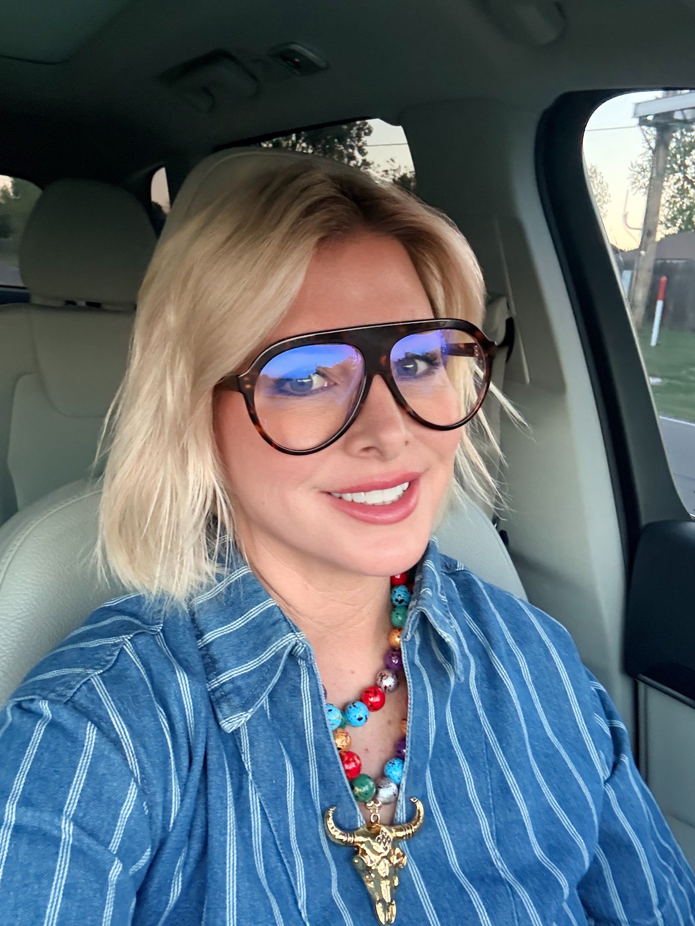 Woman with blonde bob wearing FREYRS MAXWELL bluelight glasses with tortoise frames, a blue striped shirt, and a colorful