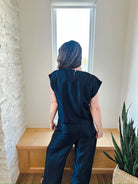 Back view of a woman wearing a navy shimmer short sleeve top and matching wide-leg pants. The top has a button closure at